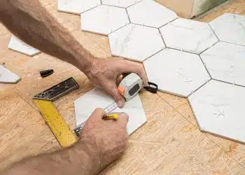 Interior finishing worker (tiler) laying white hexagon ceramic gres tiles on the floor. Bathroom renovation works. Handyman at work.